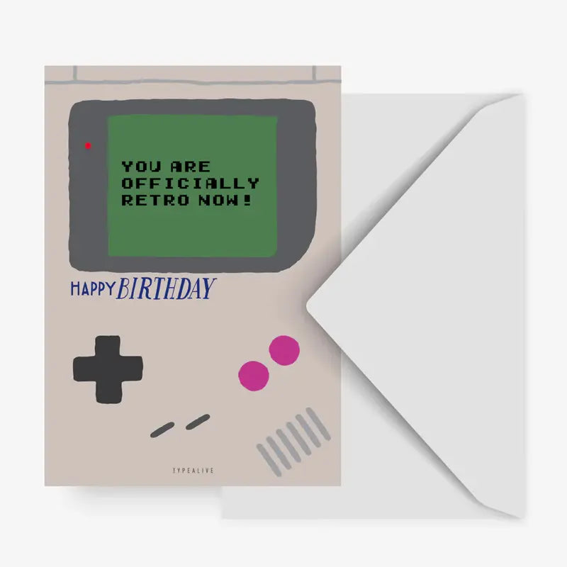 Die Typealive Postkarte "Officially Retro" Geburtstagskarte ähnelt einer Retro-Handheld-Spielkonsole mit "YOU ARE OFFICIALLY RETRO NOW!" auf dem Bildschirm und "HAPPY BIRTHDAY" in blauer Schrift darunter, abgebildet neben einem offenen weißen Umschlag.