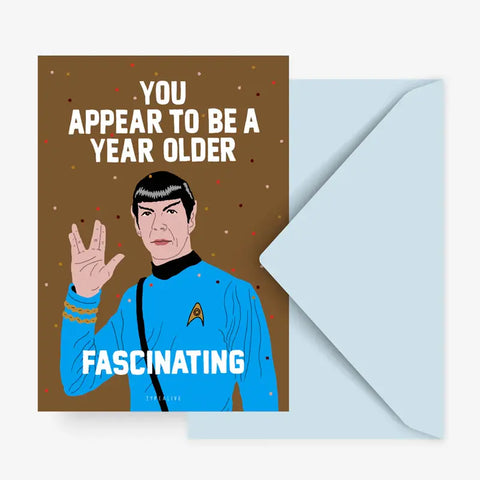 Die Typealive Postkarte "Year Older Fascinating" zeigt eine illustrierte Figur in einer blauen Star Trek Uniform, die den vulkanischen Gruß zeigt, mit der Botschaft: Du scheinst ein Jahr älter zu sein. Faszinierend. Ein offener hellblauer Umschlag liegt bei.